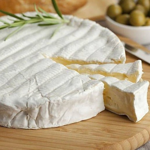 Brie cheese with 2 slices cut into it, herbs on top and olives in the background 